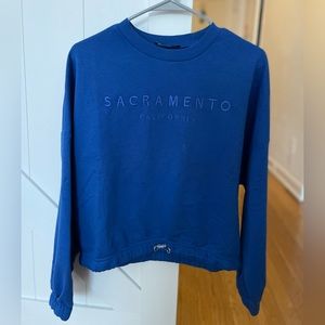 Blue sweatshirt with a tie at the bottom of it.